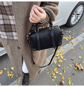 Detailaufnahme der schwarzen Plissee-Boston-Tasche mit Goldbeschlägen im herbstlichen Design