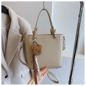 Close-up of beige lychee leather tote bag with knotted handle and plush bear charm