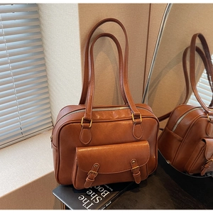 Detailed view of a vintage brown PU leather shoulder bag with double buckles on a book