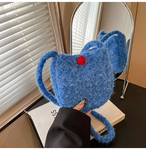 Close-up of blue plush bucket bag featuring soft faux fur and red pom-pom detail
