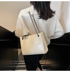 Detail view of cream white tote bag with V-quilted stitching and dark metal chain strap