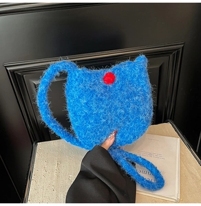 Detail of royal blue plush bucket bag with fuzzy texture and red pompom accent