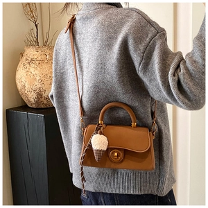 Detail der braunen Kunstlederhandtasche mit goldenem Drehverschluss und Plüsch-Anhänger