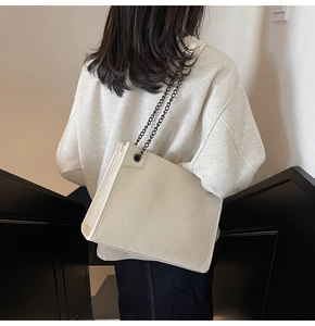 Detail of cream tote bag featuring V-shaped quilting and dark metal chain strap on model