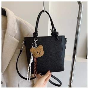 Close-up of black lychee leather bucket bag with cute bear charm and woven cord detail