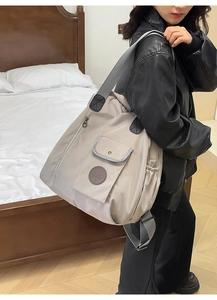 Detail of grey nylon tote bag showing flap pocket, brand logo, and wide shoulder strap