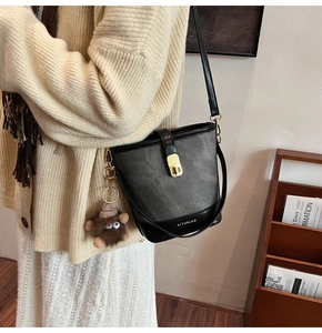 Detail of grey bucket bag with contrast stitching, gold clasp, and plush mascot charm