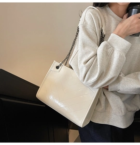 Detail view of cream tote bag featuring V-shaped quilting and metallic chain strap