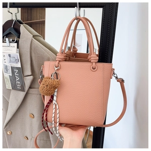 Detail of pink lychee leather bucket bag with teddy bear charm and knotted handles