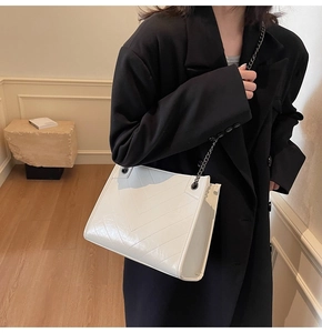 Detail of white quilted tote bag with V-shaped stitching and dark metal chain strap