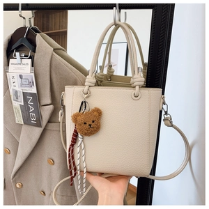 Detail of cream lychee textured tote bag with knotted handle and plush bear charm