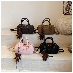Close-up of four colors of Boston bags with bear charms on stone stairs display