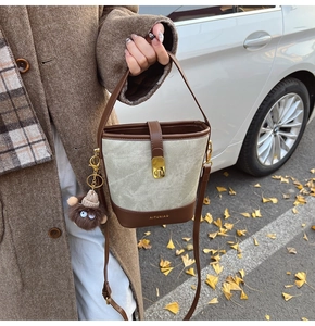 Close-up of a vintage grey bucket bag with brown leather trim and a cute plush charm