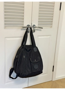 Detail of black nylon backpack hanging on door showing top handle and front buckle pocket