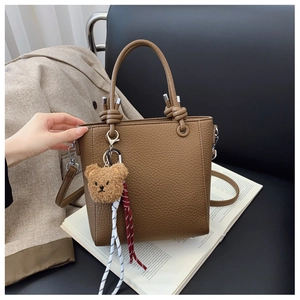 Detail of brown pebbled leather handbag featuring twin handles and a cute bear charm