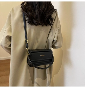 Detalle de bolso caja negro minimalista con correa ajustable y herrajes dorados