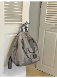 Light grey nylon backpack with wide straps and side pockets hanging on a white door
