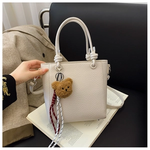 Detail of creamy white litchi grain leather tote with bear charm and knotted handle