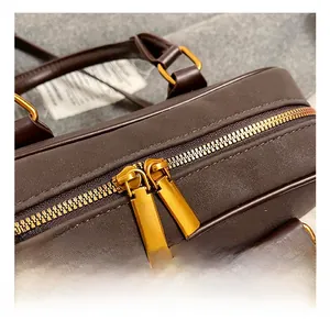 Macro shot of gold double zipper hardware on a dark brown textured leather bag