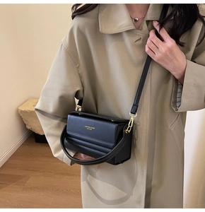 Detail of minimalist black crossbody bag featuring gold lettering and leather texture