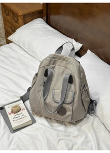 Nylon backpack side view showing elastic pockets and zippers in a cozy home setting