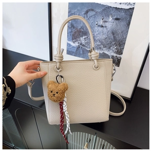 Detail of cream bucket bag in lychee texture with teddy bear charm and braided ropes