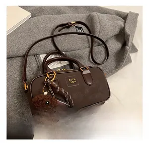 Detail of vintage brown leather boston bag with plush bear charm on grey wool coat