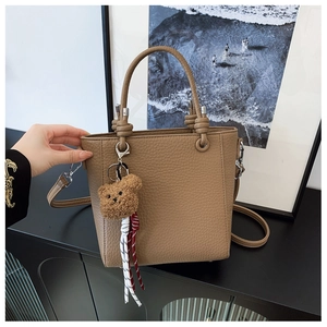 Brown bucket bag detail showing lychee grain texture and cute bear pendant accessory