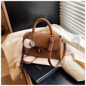 Detail der braunen Lederhandtasche mit goldener Schließe und Eiscreme-Anhänger