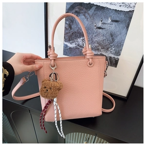 Detailed view of pink lychee leather handbag with knot handles and cute bear charm