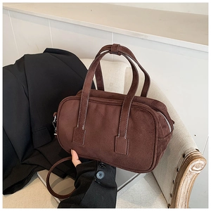 Close-up of matte dark brown handbag featuring white contrast stitching and silver zipper