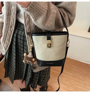 Detail of canvas bucket bag with black leather base and plush monster charm decoration