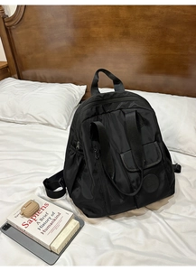 Detailed view of black waterproof nylon backpack on a white bed with lifestyle props