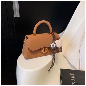 Detail der karamellfarbenen Trapez-Tasche mit goldenem Drehverschluss und Anhänger