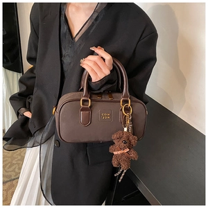 Close-up of a dark coffee Boston bag with gold hardware and a cute teddy bear charm