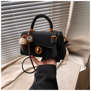 Details einer schwarzen Wildleder-Handtasche mit goldener Schließe und Anhänger