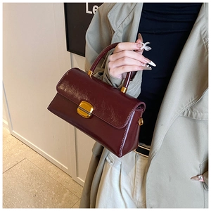 Dettaglio borsa vintage rosso scuro lucida con chiusura a scatto dorata e manico superiore