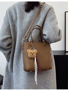Brown litchi leather bucket bag with top handles and cute bear charm shown on model