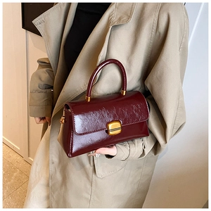 Dettaglio borsa a mano bordeaux lucida con chiusura dorata e texture vintage raffinata