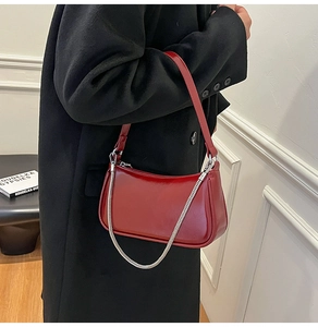 Detail der roten glänzenden Schultertasche mit Silberkette getragen auf schwarzem Mantel