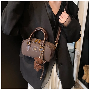Detail of coffee brown leather Boston bag featuring a plush bear charm and crossbody strap