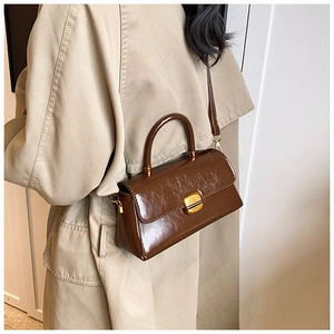 Borsa a mano in pelle verniciata marrone con chiusura dorata indossata da modella