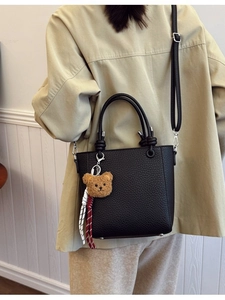 Women's black litchi pattern bucket bag with cute bear charm shown on a model