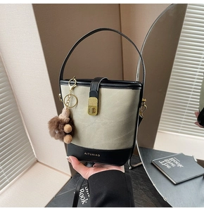 Detail of beige canvas and black leather bucket bag with gold hardware and plush charm