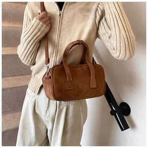 Model wearing a dark brown matte leather crossbody bag with dual handles and silver hardware