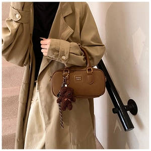 Detail view of a vintage brown leather pillow bag with a plush bear charm and metal logo