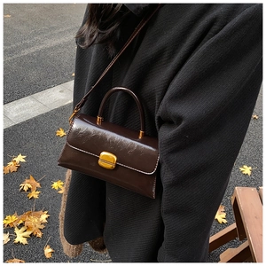 Dettaglio borsa a tracolla marrone scuro vintage indossata su un cappotto nero strutturato