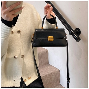 Borsa a tracolla nera lucida con manico rotondo in metallo su cardigan in maglia beige