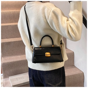 Dettaglio di una borsa a tracolla in pelle nera lucida con chiusura vintage oro