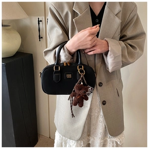 Detail of black leather Boston bag with gold logo and cute brown teddy bear charm